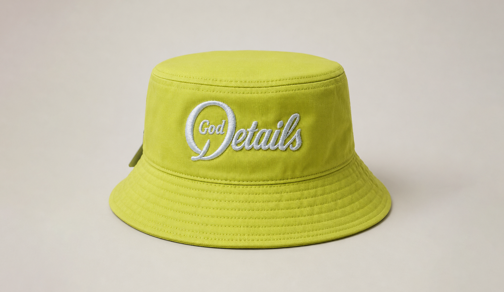 Yellow bucket hat with 'God Details' embroidery on a beige background