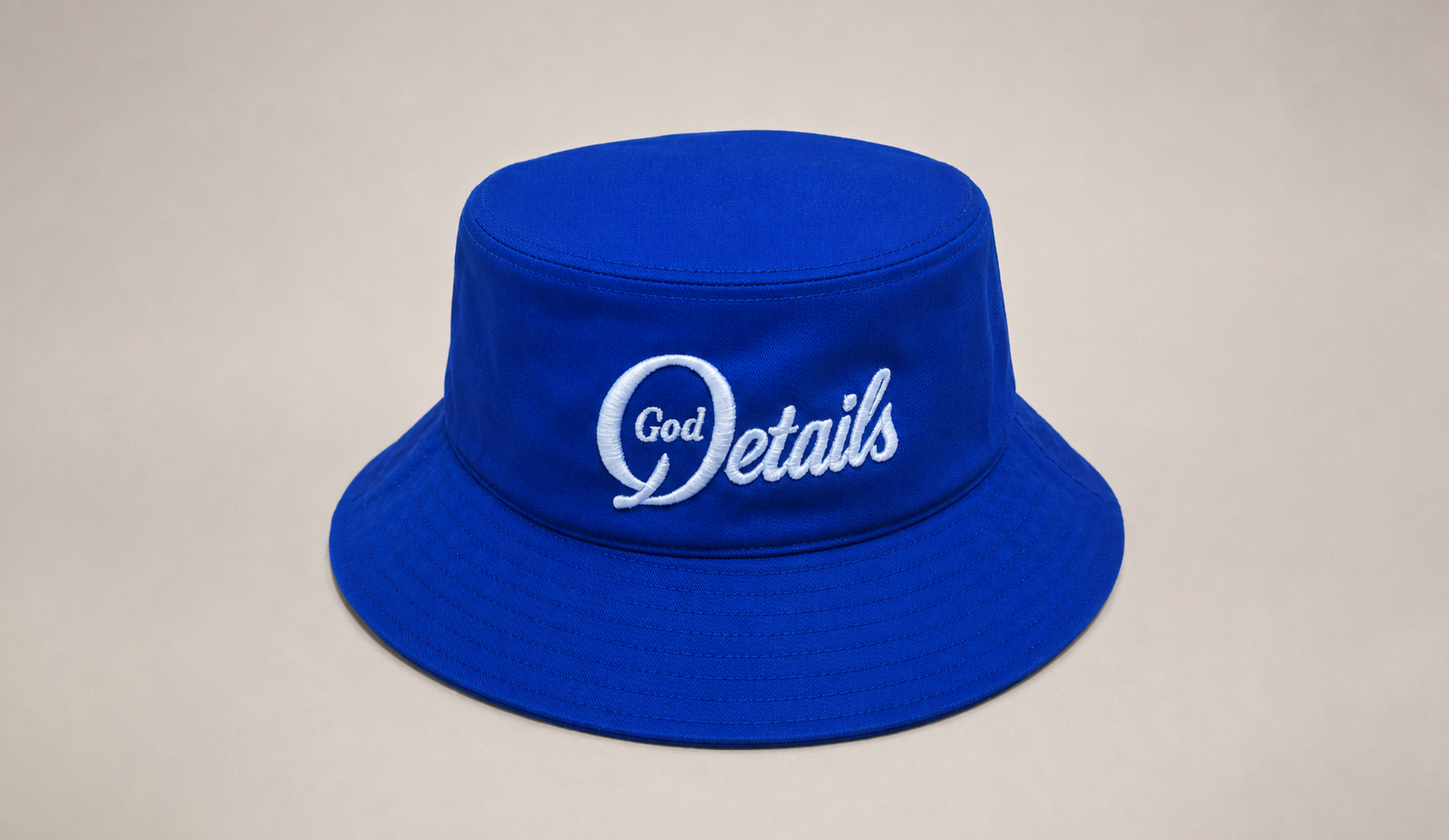 Blue bucket hat with 'God Details' text on a beige background