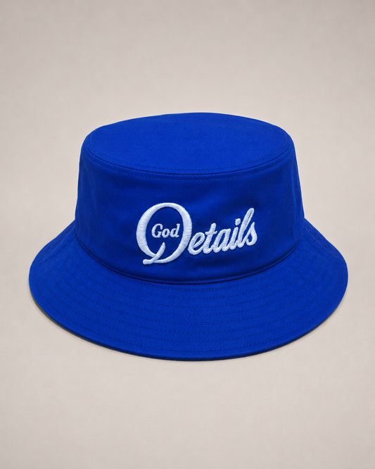Blue bucket hat with 'God Details' text on a beige background